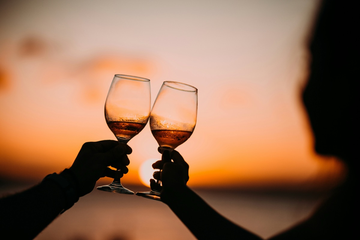 Two glasses raised against a sunset over the water